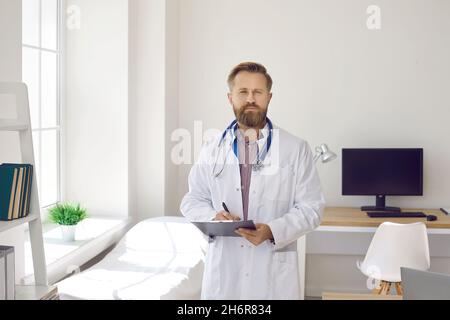 Porträt eines ernsthaften männlichen Arztes, der im medizinischen Büro steht und die Zwischenablage hält Stockfoto