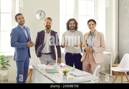 Gruppenporträt von glücklichen kreativen Geschäftsleuten, die während eines Arbeitsmeeting am Schreibtisch stehen Stockfoto