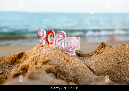 Abbildungen 2022 vor dem Hintergrund von Küstenwellen durch Meer oder Meer mit Karamellrohr. Reisen Sie während der Quarantäne am Silvesterabend, vor der Ankunft neuer Stockfoto