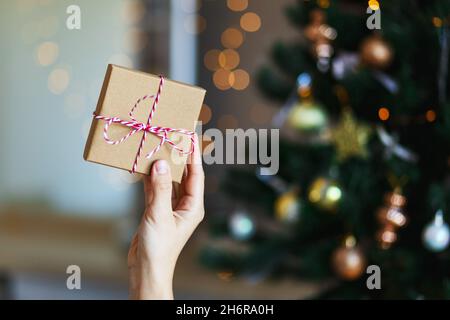 Weihnachten Öko-Geschenk in Frau Hand. Leuchtendes Bokeh, Tannenbaum Hintergrund. Winterurlaub . Kein Abfall, frei von Kunststoff. Stockfoto