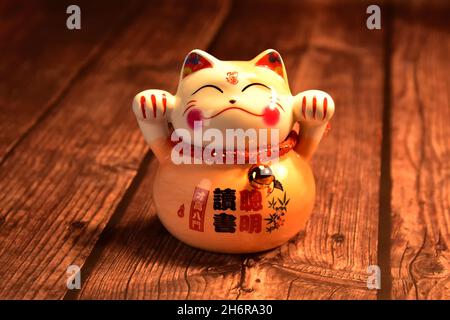 Eine japanische Glückskatze (Maneki neko) aus Porzellan auf einem rustikalen Holztisch. Stockfoto