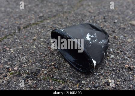 Zerknittert eine Papierkaffeetasse auf Asphalt. Weggeworfene Einweg-Kaffeetasse mit Kunststoffdeckel auf der Straße. Becher aus zerkleinertem Papier. Abgebrochener Müll Stockfoto