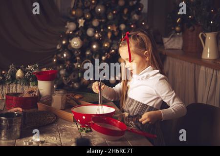 Das Mädchen in der Küche bereitet Kekse zu. Weihnachtsschmuck, Familientraditionen, Weihnachtsessen, Feiertagsabend. Stockfoto