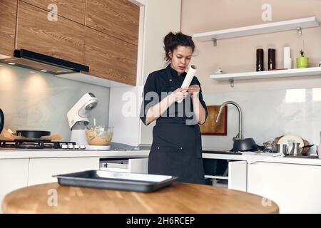 Junge schöne Mischrassen Frau breitet Gebäck Papier auf einem Teller in der hellen modernen Küche Stockfoto