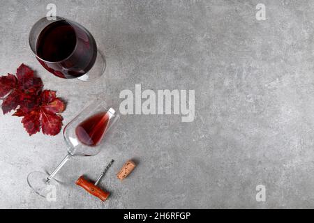 Draufsicht auf Rotweingläser mit roten Herbsttraubenblättern und Korkenzieher und Weinstopfen auf grauem Steintisch Stockfoto