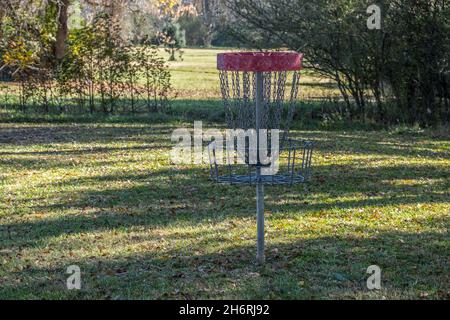 Nahaufnahme eines leeren Golfscheibenkorbs im Schatten, umgeben von heruntergefallenen Blättern, an einem sonnigen Tag im Herbst in einem Park Stockfoto