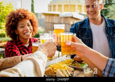 Eine Gruppe von multiethnischen, glücklichen Freunden, die einen gesunden Lebensstil leben und sich beim Biertrinken im Pub-Restaurant im Freien entspannen - Junge Menschen genießen Getränke Stockfoto