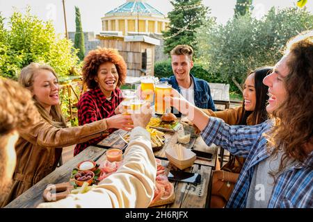 Eine Gruppe von multiethnischen, glücklichen Freunden, die einen gesunden Lebensstil leben und sich beim Biertrinken im Pub-Restaurant im Freien entspannen - Junge Menschen genießen Getränke Stockfoto