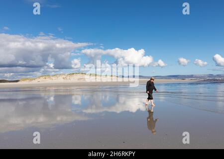 Ein erwachsener Mann mit Hut, der an einem Sandstrand entlang läuft. Stockfoto