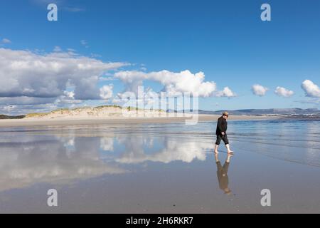 Ein erwachsener Mann mit Hut, der an einem Sandstrand entlang läuft. Stockfoto