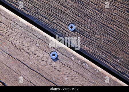 Schrauben und Nägel an zwei Holzstufen verschiedener Bäume auf der Promenade Stockfoto