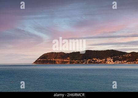 Blick von Alassio auf das Vorgebirge von Capo Mele mit dem Fischerdorf Laigueglia bei Sonnenuntergang, Savona, Ligurien, Italien Stockfoto