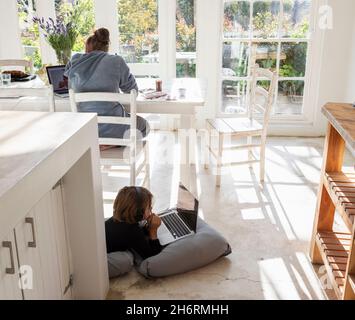 Acht Jahre alter Junge, der auf Kissen liegt, sich an den Händen kinn, einen Laptop-Bildschirm ansieht, Hausaufgaben macht. Stockfoto