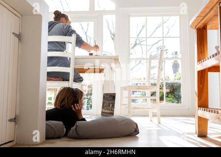 Acht Jahre alter Junge, der auf Kissen liegt, sich an den Händen kinn, einen Laptop-Bildschirm ansieht, Hausaufgaben macht. Stockfoto