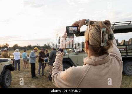 Rückansicht einer Frau, die ein Smartphone-Foto von einer Gruppe von Menschen auf einer morgendlichen Pirschfahrt gemacht hat Stockfoto