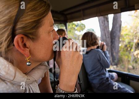 Familie in einem Jeep während einer Fahrt durch Buschland mit Fernglas und Kamera Stockfoto