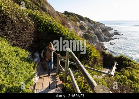 Erwachsene Frau, die über einem Strand die Stufen zur Klippe hinauf läuft. Stockfoto