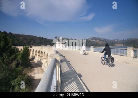 Los Angeles, CA, USA - 17. November2021: Zwei Radfahrer fahren über den Lake Hollywood über den Mulholland-Staudamm in Los Angeles, CA. Stockfoto