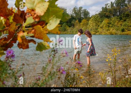 Ein kleiner Junge und ein Mädchen stehen zusammen und watet im Sommer in einem See Stockfoto