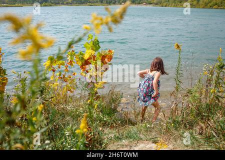 Das kleine Mädchen steht im Sommer am Rande der Prärie und watend im See Stockfoto