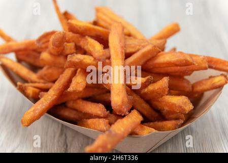 Knusprige Beilage mit Pommes Frites aus Süßkartoffeln, die in einem Pappboot serviert werden, um sie unterwegs zu essen. Stockfoto