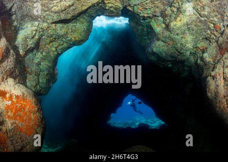 Das Sonnenlicht dampft von einem Oberlicht in der Spitze dieser Höhle vor der Kona Coast of the Big Island, Hawaii. Ein Taucher (MR) ist am Eingang c eingerahmt Stockfoto