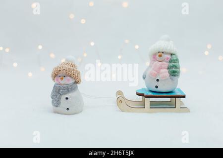 Dekorative Figuren im Weihnachtsstil. Zwei Statuette eines Schneemanns in einem gestrickten Hut auf dem Schlitten. Stockfoto
