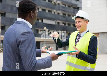 Der Baumeister gibt dem neuen afroamerikanischen Geschäftsmann die Schlüssel Stockfoto