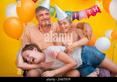 Familienportrait auf gelbem Hintergrund. Das Mädchen legte sich auf die Knie ihrer Eltern Stockfoto
