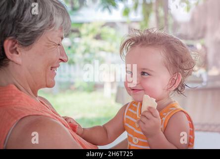 Das Kind in den Armen der Großmutter hält einen Keks in ihren Händen Stockfoto