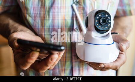 Nahaufnahme des mittleren Abschnitts eines unbekannten Mannes, der eine Überwachungskamera und ein Mobiltelefon in der Hand hält, um einen Kopierplatz für die Vorderansicht einer App zu installieren Stockfoto