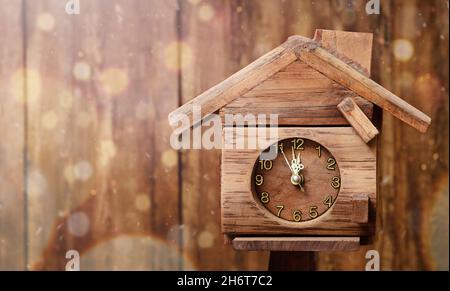 Eine Uhr in Form des Hauses zeigt Mitternacht auf dem Hintergrund der Holzwand Stockfoto