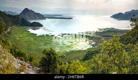 Blick von einer kurvenreichen Bergstraße nicht lange nach Sonnenaufgang im Frühherbst, da Sonnenlicht die Oberfläche des Nockenwassers reflektiert. Stockfoto