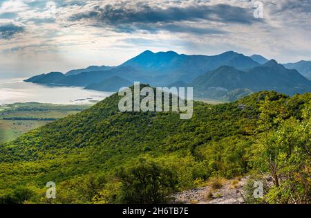 Blick von einer kurvenreichen Bergstraße nicht lange nach Sonnenaufgang im Frühherbst, da Sonnenlicht die Oberfläche des Nockenwassers reflektiert. Stockfoto