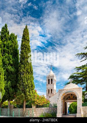 Kleine serbisch-orthodoxe Kirche, umgeben von hohen grünen Bäumen im September in der Nähe des Skadar-Sees, in den Bergen, mit blauem Himmel und wispy weißen Wolken. Stockfoto