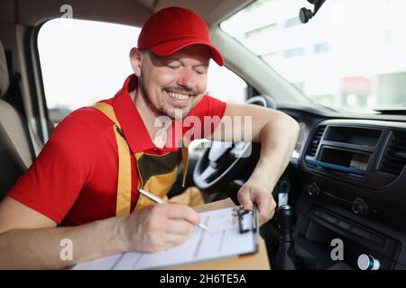 Lächelnder Lieferdienstmitarbeiter füllt die erforderlichen Dokumente nach dem Versand aus Stockfoto