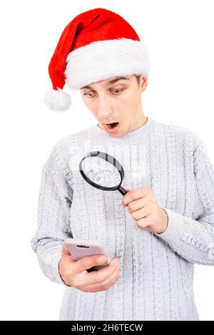 Überrascht junger Mann in Santa hat mit einem Vergrößerungsglas Blick auf das Handy auf dem weißen Hintergrund Stockfoto