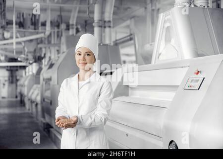 Anlagenbetreiber Ingenieur Mühle vor dem Hintergrund der modernen Ausrüstung hält Frau Weizenkorn in den Händen. Stockfoto