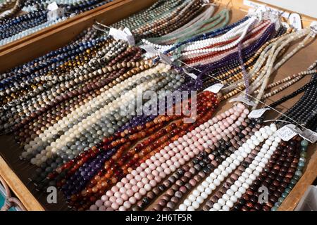 Perlenhalsketten in verschiedenen Farben und Typen, einige mit Preisschild, stehen nebeneinander in einer Holzkiste, die in einem Marktstand zum Verkauf steht Stockfoto