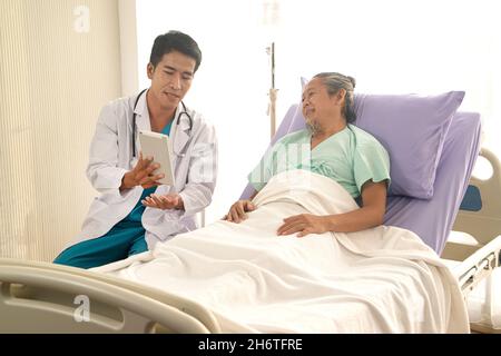 Asiatischer männlicher Arzt erklärt Diagnose und zeigt auf Tablette für ältere asiatische Patienten. Stockfoto