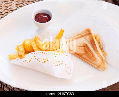 Pommes frites, Sandwiches mit Käse und Schinken und Tomatenketchup auf einem weißen Teller. Stockfoto