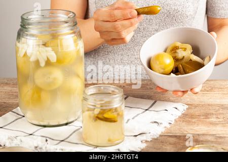 Eine junge kaukasische Frau isst selbstgemachtes eingelegtes Gemüse. Sie nimmt eine Gurke aus einer Schüssel mit Tomaten und Gurken. Stockfoto