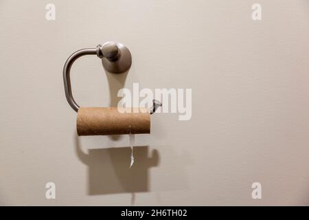 Konzeptbild mit einem Toilettenpapieraufhänger und einer leeren Toilettenpapierrolle, die darauf hängt. Nützliches Bild für Mangel im Zusammenhang mit gestörter Versorgungskette Stockfoto