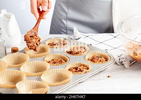 Herstellung von köstlichen Obst und Nuss Cupcake auf weißem Marmor Arbeitsplatte Hintergrund. Muffin-Dose mit Liner, Zutaten und Utensilien sind zu sehen. Eine Frau ist es Stockfoto