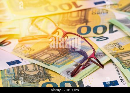 Brille auf dem Hintergrund des europäischen Geldes im Sonnenlicht. Selektiver Fokus. Stockfoto