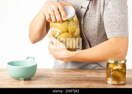 Eine kaukasische Köchin mit Schürze versucht, einen hartnäckigen Glasdeckel zu öffnen. Sie wendet Gewalt an, um den Deckel in der Küche abzuschrauben. Konzeptbild zum Beizen nach Stockfoto