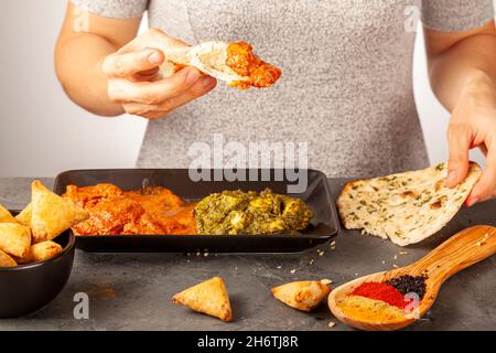 Eine Frau isst leckeres indisches Essen mit verschiedenen Gerichten. Sie taucht Naan-Brot in ein frisches Brot. Konzept für die Vielfalt der asiatischen Küche. Tikka Masala und Stockfoto