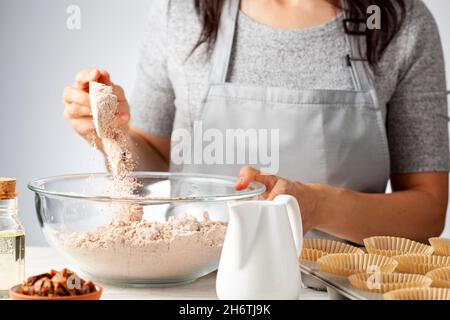 Eine Frau fügt Zutaten für die Herstellung von köstlichem Obst und Nusskuchen auf weißem Marmor Arbeitsplatte Hintergrund. Muffin-Dose mit Liner, Zutaten, ein Stockfoto