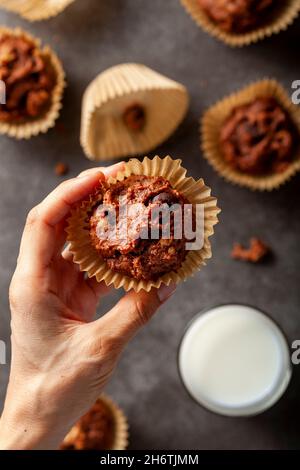 Eine kaukasische Frau hält eine frisch gebackene köstliche Schokoladennuss-Muffins auf grauem Hintergrund mit einem Glas Milch zum Dunkeln serviert. Konzept f Stockfoto