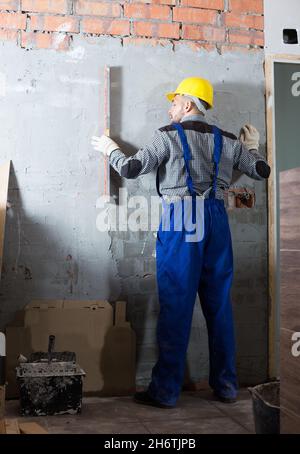 Männlicher Arbeiter im Helm misst die Wand Stockfoto